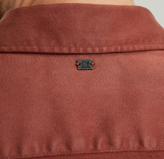 Detail van de kraag van een koraalrood overhemd met een metalen logo patch.