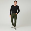 Man met een zwarte longsleeve en groene corduroy jeans, staand.