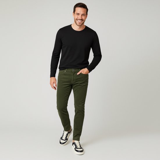 Man met een zwarte longsleeve en groene corduroy jeans, staand.