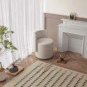 Lichtbeige, ronde kruk met een gebogen rugleuning, geplaatst in een woonkamer bij een open haard.