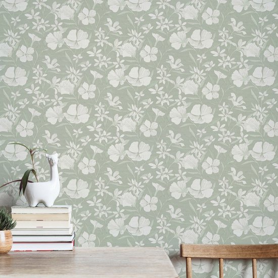 Lichtgroen behang met een delicaat wit bloemen- en bladerenpatroon, getoond op een muur met een houten tafel.