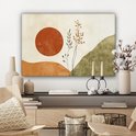 Abstract schilderij met oranje zon, takken en groene heuvels, hangend boven een dressoir.
