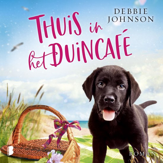 Een zwarte puppy zit naast een picknickmand op een deken aan zee. Tekst: Thuis in het Duincafé. Debbie Johnson.