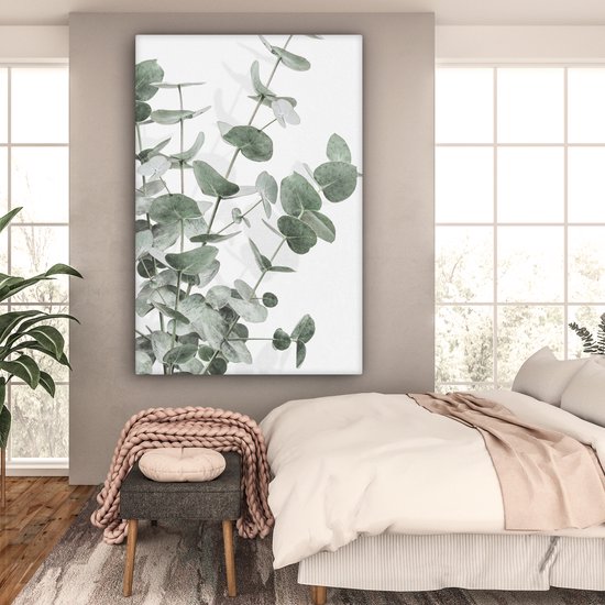 Canvas van eucalyptusbladeren in een slaapkamer met een bed en grote ramen.