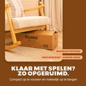 Bruine kartonnen doos van een speeltent onder een schommelstoel. Tekst: KLAAR MET SPELEN? ZO OPGERUIMD.