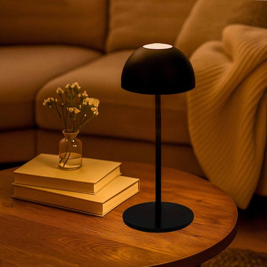 Lampe de table LED noire et dimmable avec base et abat-jour ronds, éclairée sur une table en bois.