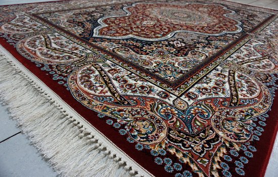 Hoek van een rood Perzisch vloerkleed met witte franjes. Het kleed is versierd met gedetailleerde bloemenpatronen in diverse kleuren en traditionele ornamenten.