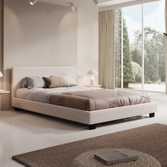 Lit avec un cadre et une tête de lit en tissu côtelé beige. Couvre-lit matelassé marron et coussins décoratifs beiges.
