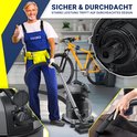Man met blauwe overall geeft duim omhoog bij een industriële stofzuiger in een garage met fietsen.
