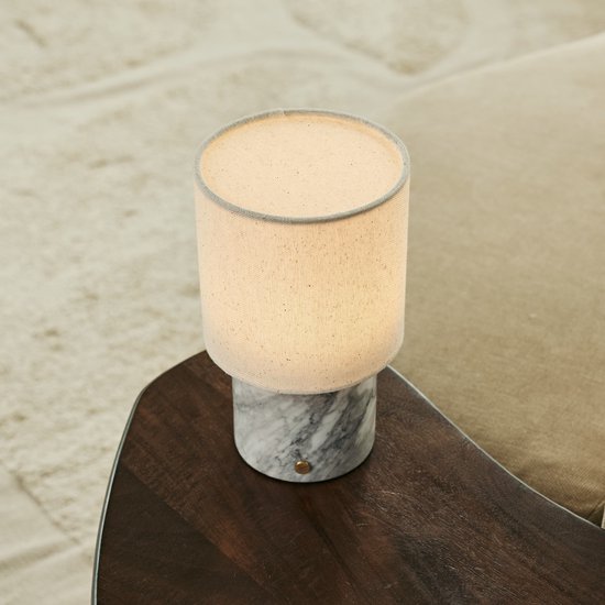 Tafellamp met marmeren voet en linnen kap, op een houten tafel.