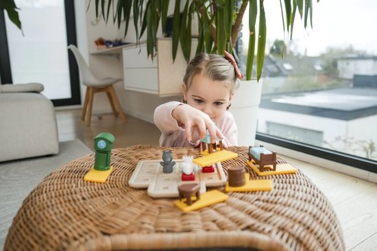 Une jeune fille avec un ruban rouge dans les cheveux joue avec le jeu 'Le Loup et les 7 Chevreaux Deluxe'.