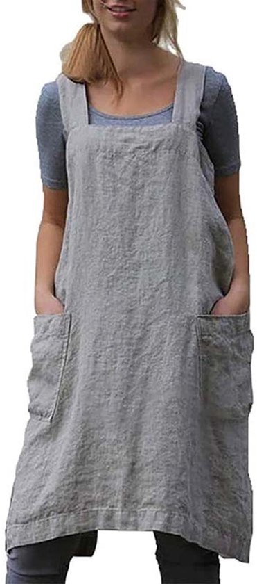 Femme portant un tablier uni en lin gris avec de larges bretelles croisées et quatre grandes poches.