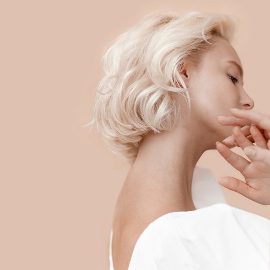 Zijaanzicht van een vrouw met kort, blond, golvend haar en witte top.