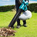 Man gebruikt turquoise Makita bladblazer in een tuin met herfstbladeren.