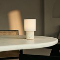 Tafellamp met beige linnenkap en travertijnen voet op een ronde tafel.