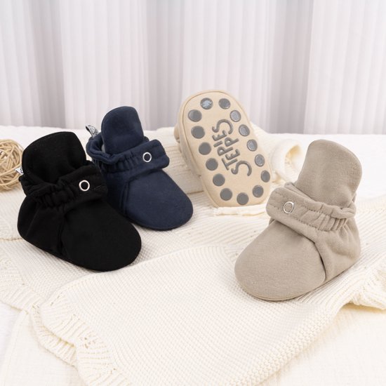 Set van vier babyslofjes in zwart, donkerblauw, beige en lichtbruin met zilverkleurige 'STEPPIES' opdruk.
