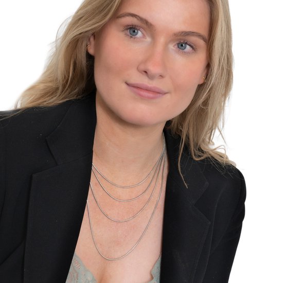 Jonge vrouw met blauwe ogen en blond haar, draagt meerdere zilverkleurige slangenkettingen op verschillende lengtes.