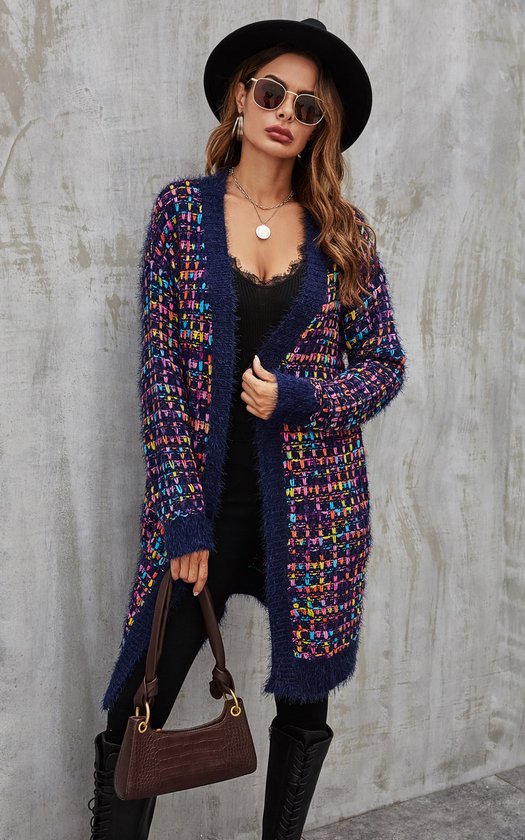 Model draagt lang marineblauw vest met gekleurde spikkels en pluizige randen, zwarte top, broek en hoed.