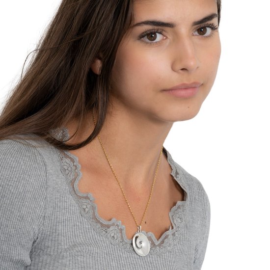 Model draagt een gouden ketting met een ronde hanger met een halve maan erop.
