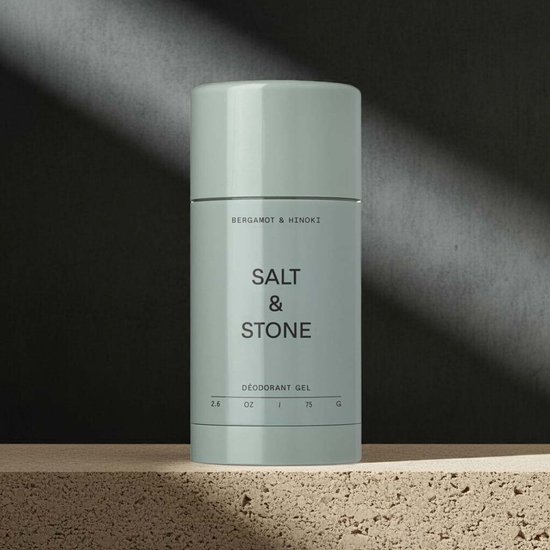 Lichtgroene deodorantstick van Salt & Stone, staat op een stenen plateau met donkere achtergrond. Tekst: "BERGAMOT & HINOKI SALT & STONE DÉODORANT GEL 2.6 OZ 75 G".