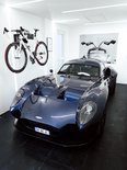 Witte racefiets met een Stasdock muurbeugel, naast een donkerblauwe sportauto met open deuren.