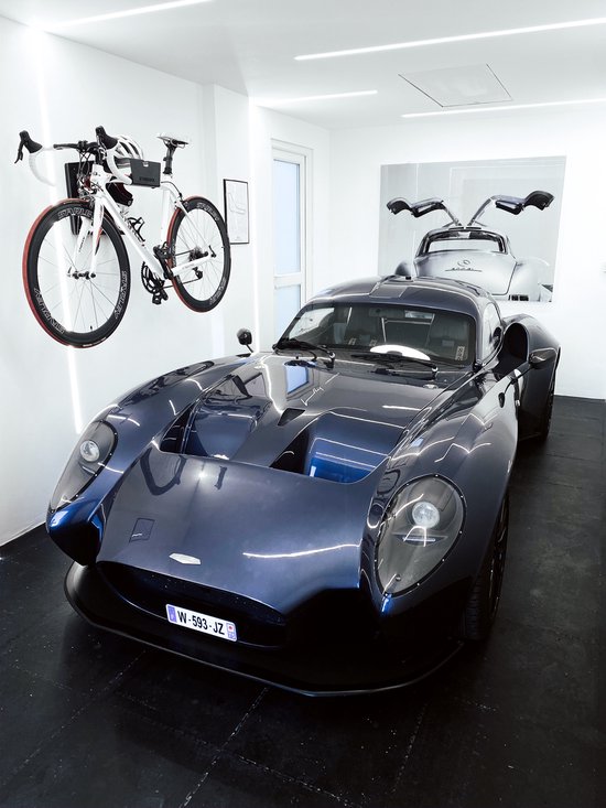 Witte racefiets met een Stasdock muurbeugel, naast een donkerblauwe sportauto met open deuren.