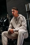 Man zittend met beige Gorilla Wear trainingspak in de sportschool.