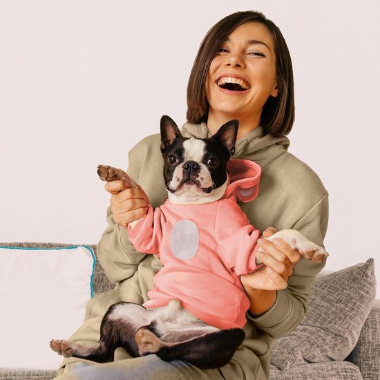 Lachende vrouw houdt een Boston terriër vast die een roze hoodie met oortjes draagt.