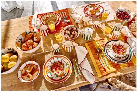 Gedekte tafel met servies in de kleur geel en groen met strepen, inclusief mokken, schalen en borden.
