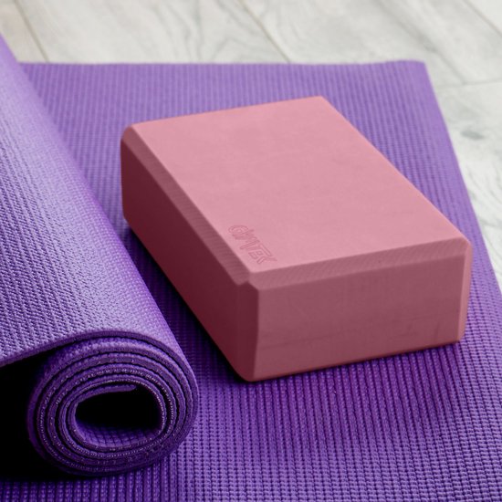 Roze yogablok op een paarse yogamat met een opgerolde paarse mat ernaast.