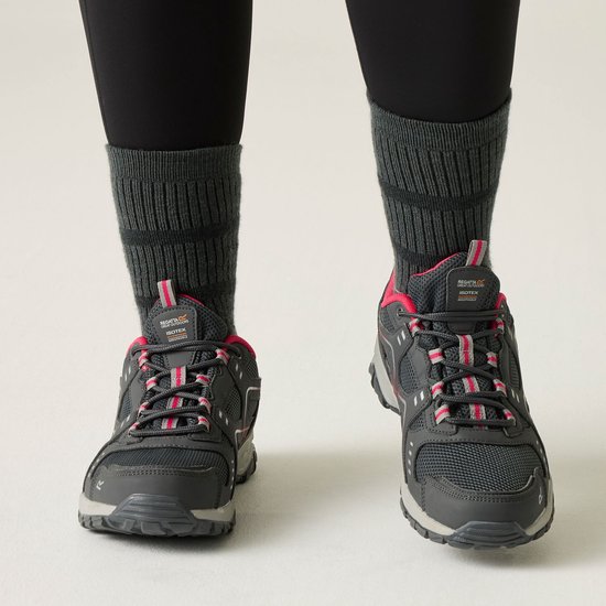 Pieds de femme en chaussettes grises et chaussures de randonnée noires imperméables avec accents roses, vues de face.