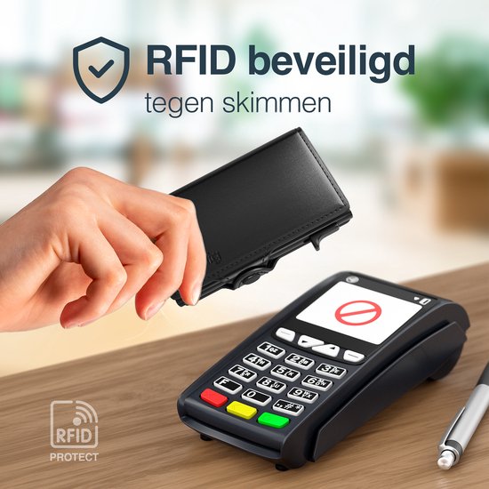 Main tenant un portefeuille Hëndig noir avec protection RFID près d'une borne de paiement.