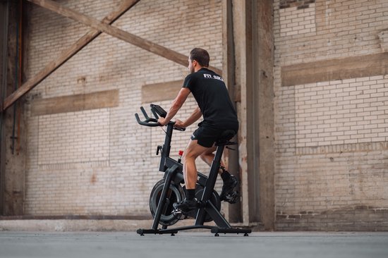 Man met zwarte kleding traint op een zwarte spinfiets in een industriële omgeving.