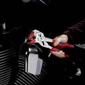 Hand houdt een tang met rode en blauwe handvatten vast, die een deel van een motorfiets aanpast.