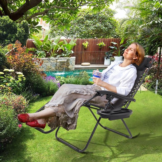 Vrouw met een drankje, ontspannen in een zwarte ligstoel met bijzettafel in een zonnige tuin bij een zwembad.