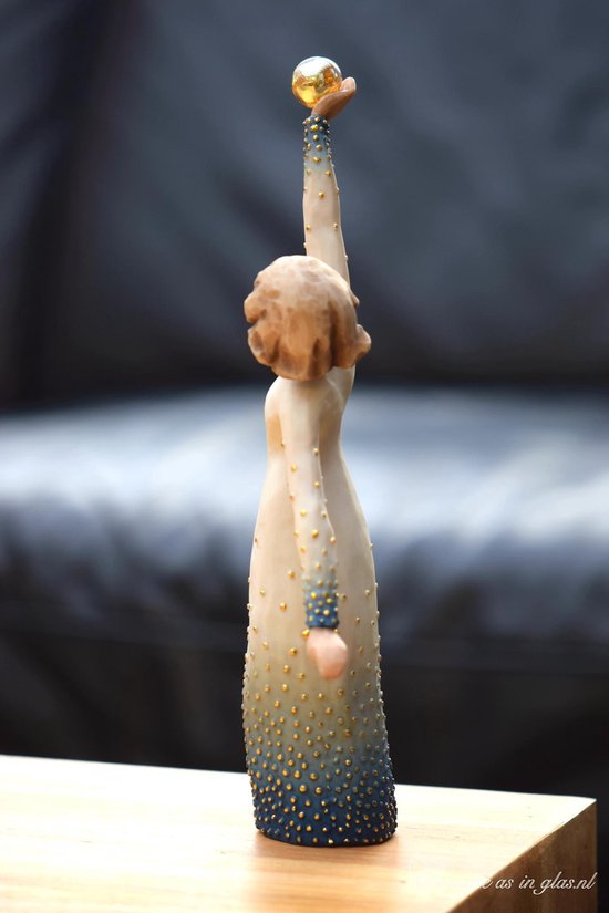Een Willow Tree beeldje van een vrouw in een witte jurk met gouden stippen, die een gouden bol omhoog houdt.