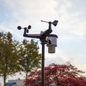 Alecto weerstation met windmeter, regenmeter en windvaan tegen een achtergrond van bomen en herfstkleuren.