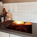 Een snijplank met een brandnetel in silhouet tegen een oranje zonsondergang, op een donker keukenblad.