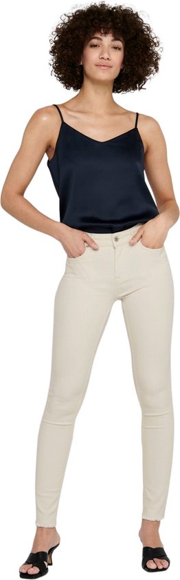 Model in een lichte, skinny jeans met rafels aan de onderkant en zwarte sandalen met hak.
