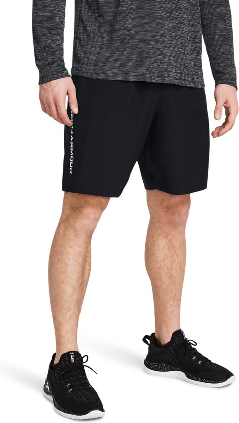 Man in zwart sportshirt met halve rits en zwart sportbroekje met logo op linkerbeen.