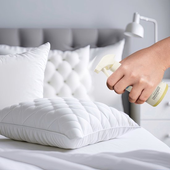 Hand spuit Sanamedi Huisstofmijt Spray op een wit gestikt kussen in een slaapkamer.