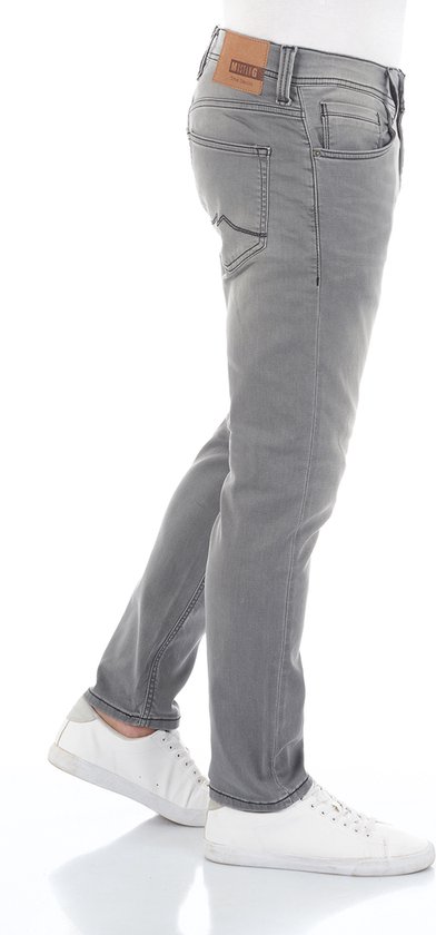 Zijaanzicht van een model in grijze jeans met witte sneakers en een leren Mustang label op de achterkant.
