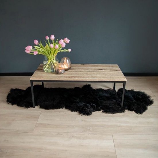 Salontafel met licht houten blad en zwart stalen frame. Een boeket roze tulpen en twee glazen windlichten erop. Zwart schapenvachtje eronder.