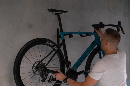 Man bevestigt blauwe racefiets met zwarte velgen aan zwarte fietsmuurbeugel.
