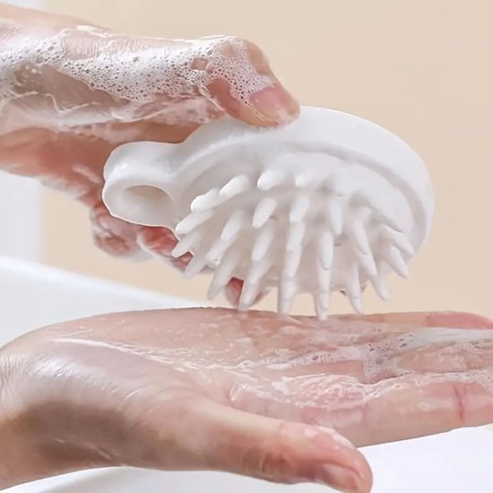 Witte hoofdhuidmassager met siliconen nopjes wordt in de hand gehouden met schuim.