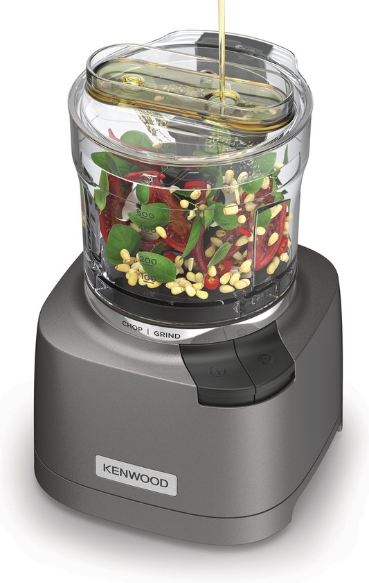 Grijze Kenwood chopper met groene kruiden en olie die wordt toegevoegd.