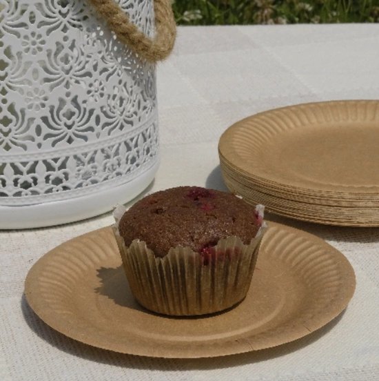 Chocolademuffin met frambozen op een bruin kartonnen bordje, naast een stapel bordjes.