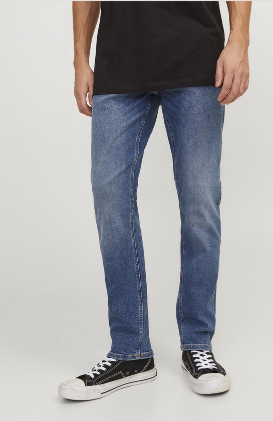 Voeten van een man in een zwarte t-shirt en blauwe jeans met canvas sneakers.