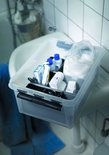 Transparante opbergbox met zwarte clips, gevuld met toiletartikelen zoals flesjes en wattenschijfjes.