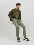 Man zittend op een barkruk, draagt olijfgroene chino broek met groen jack en t-shirt.